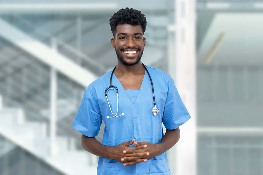 A healthcare worker in blue scrubs with a stethoscope standing in a hospital atrium.