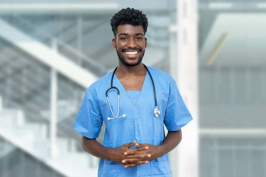 A healthcare worker in blue scrubs with a stethoscope standing in a hospital atrium.
