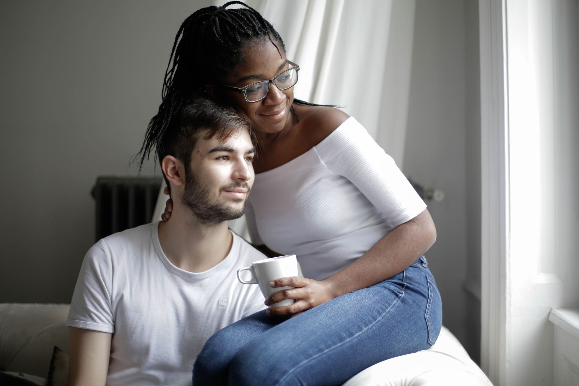 A couple relaxing together on a sofa by a bright window, one holding a mug - the £29,000 financial requirement is evidenced from the household you share, so the arithmetic has to be right before the application goes in.