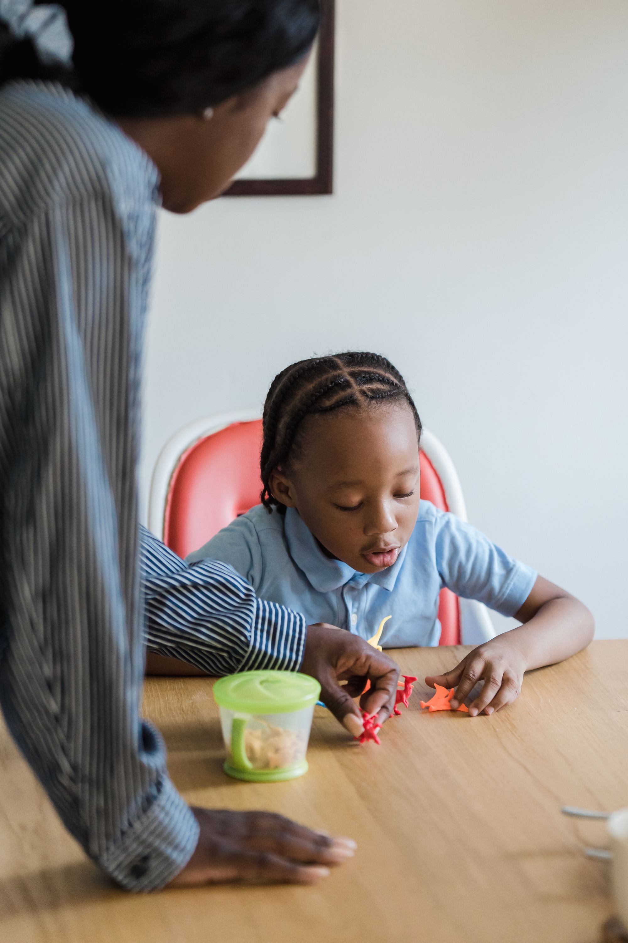 A mother leaning in beside her young child at the table as they play with toy dinosaurs together - the parent route is what secures the ongoing, active involvement in a child's life that the Home Office looks for.